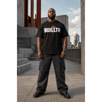 Black man wearing a Buillth Crown Logo black t-shirt with red crown wordmark, streetwear style, standing on a concrete rooftop with city skyline in the background
